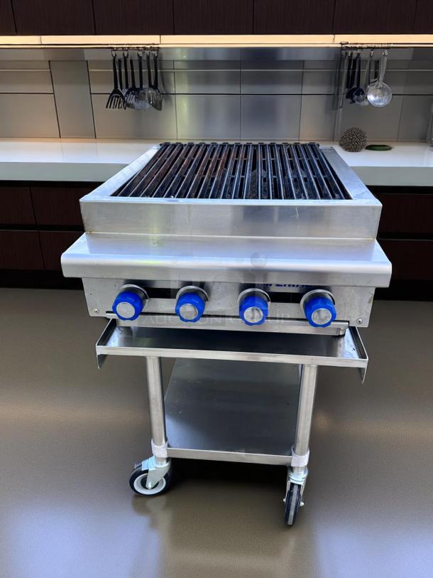 Commercial stainless steel grill with four blue knobs on a wheeled stand, featuring a large cooking surface. Excellent condition.