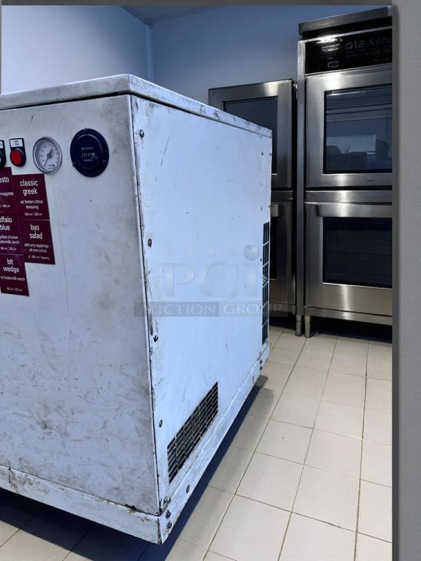 Commercial kitchen appliance with control gauge and red labels, showing wear. Stainless steel ovens in the background.