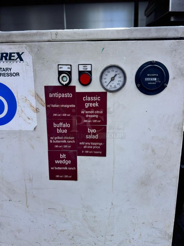 Commercial refrigeration unit with operational dials and labels listing salad options and calorie counts. Visible wear on surface.