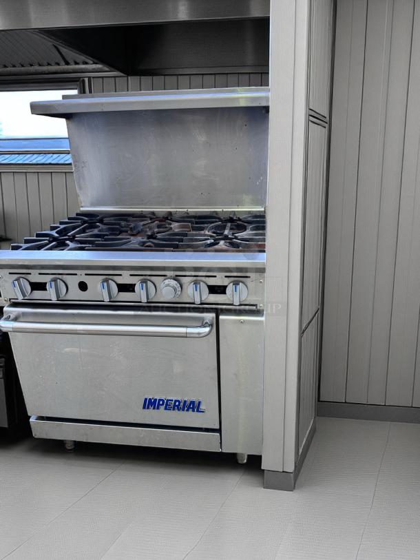 Imperial stainless steel commercial gas range with six burners, oven, and backsplash. Used condition with visible wear.