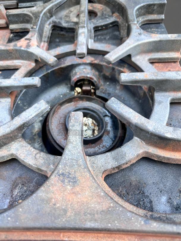 Rusty cast iron stove burner with visible wear and rust, featuring intricate grate design for vintage or repair use.