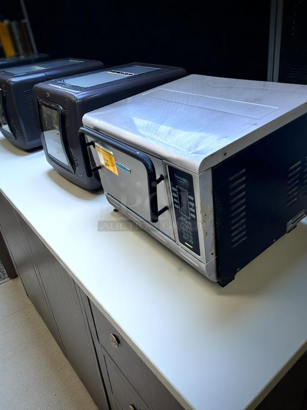 Silver Tornado commercial microwave, visibly used, with front handle and visible control panel. Displayed on countertop.