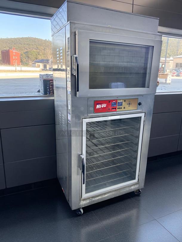 Nu-Vu stainless steel commercial oven with dual glass doors, multiple racks, visible digital controls, and caster wheels.