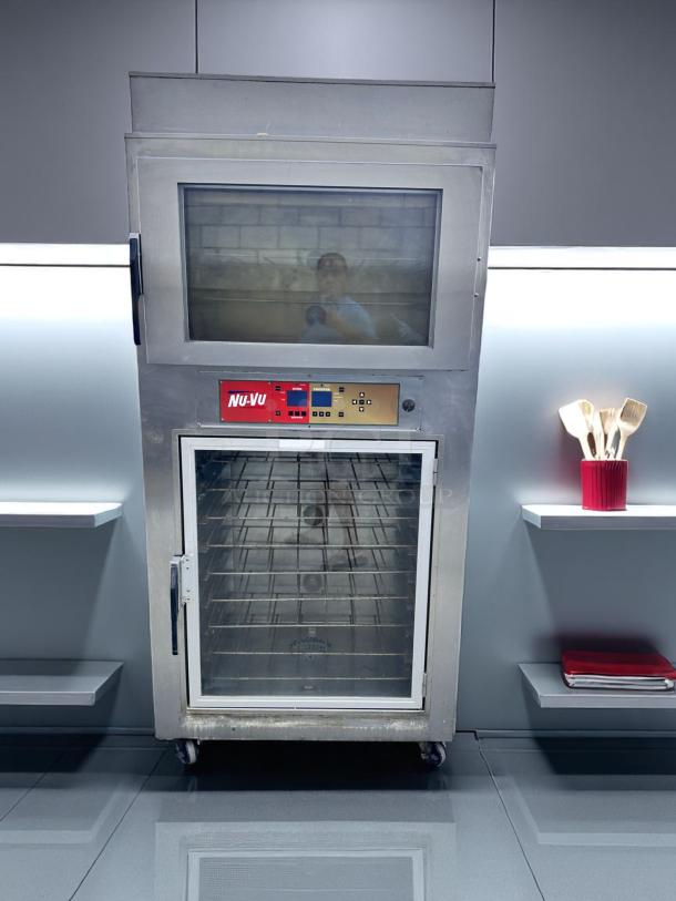 NU-VU commercial oven with glass door, stainless steel exterior, visible interior racks, control panel, on wheels, good condition.