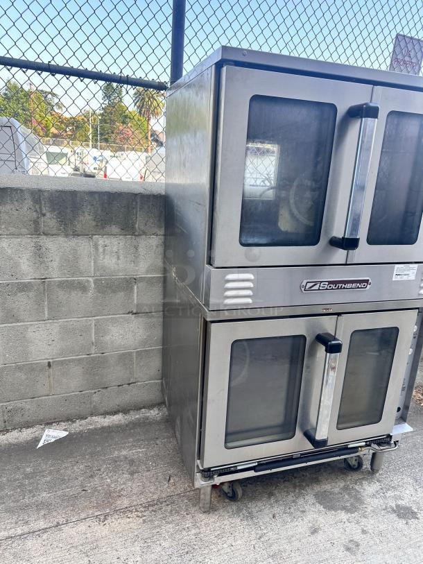 Southbend stainless steel double oven on wheels, with visible wear. Front glass doors and handles intact. Ideal for commercial use.