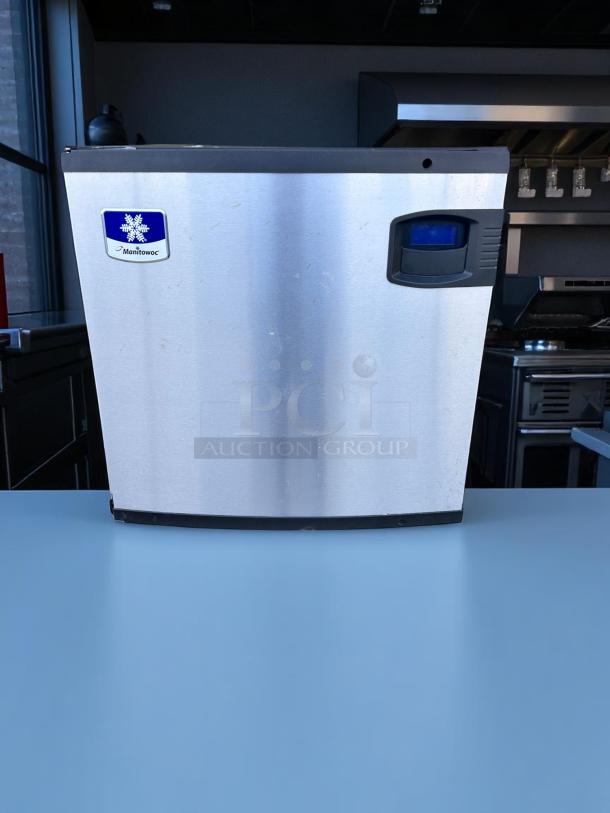 Manitowoc ice maker, stainless steel, front handle, minor surface wear, manufacturer logo visible, commercial kitchen use.