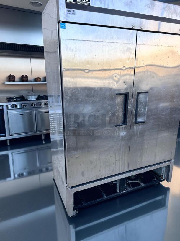 Stainless steel commercial refrigerator, double-door, scratches visible, label reads "Refrigerator", placed in a modern kitchen.