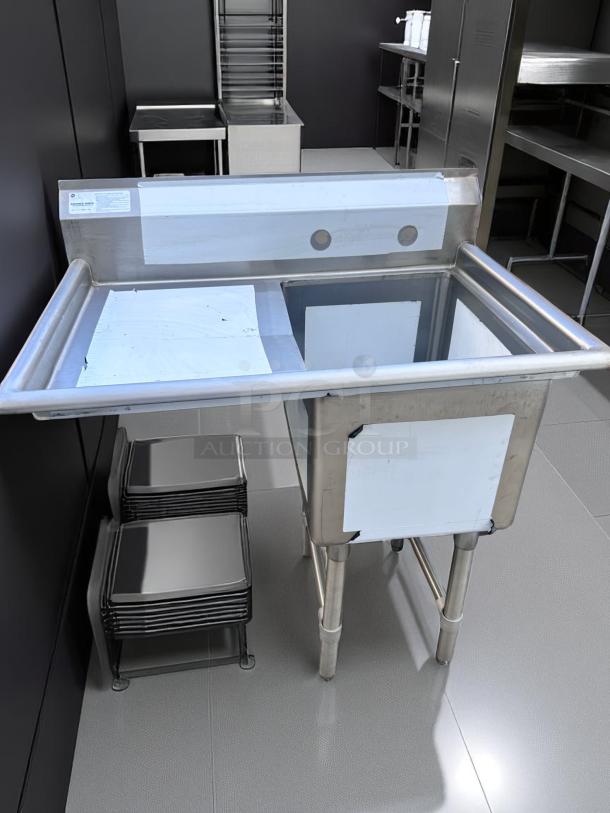 Stainless steel commercial sink with backsplash and double drainboard. Features sturdy legs; appears in good condition.