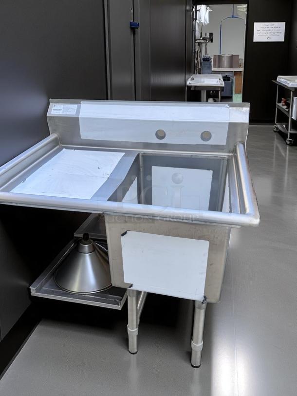 Stainless steel industrial sink with backsplash, dual faucet holes, and sturdy legs. Includes a label with specifications. Excellent condition.