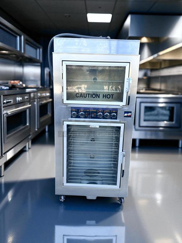 Nu-Vu stainless steel commercial oven, double-door, with "Caution Hot" label. Features controls, grills, and transparent windows.