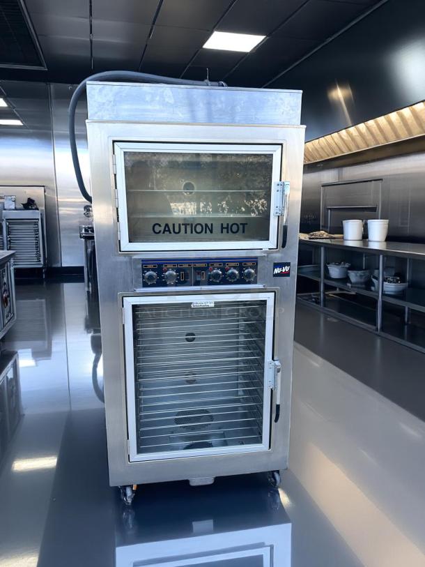 Stainless steel commercial oven with dual glass doors, labeled "CAUTION HOT." Features control panel and multiple shelves.