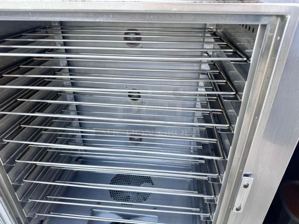 Commercial stainless steel warming cabinet interior with multiple adjustable wire racks, fan visible at the bottom, in excellent condition.