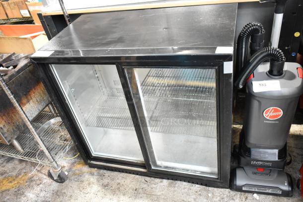 Commercial double-door glass refrigerator, black frame, used, with metal shelves; Hoover vacuum beside, model HVRPWR.