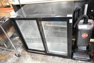 Commercial double-door glass refrigerator, black frame, used, with metal shelves; Hoover vacuum beside, model HVRPWR.