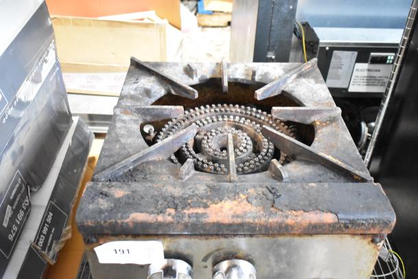 Commercial gas stove burner with rust and wear. Two control knobs visible. Auction tag number 191 attached.