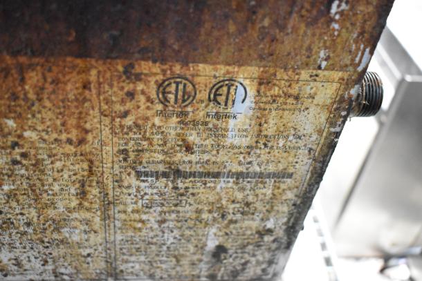 Rusty metal panel with visible ETL Intertek certification labels, indicating industrial use. Serial number partially visible.