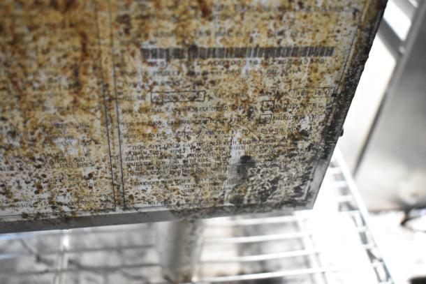 Rusted metal appliance label with unreadable markings, indicating poor condition and possible antique status.