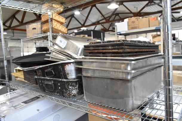 Stack of used kitchen baking trays and pans on metal shelves in an industrial setting. Auction tag visible.