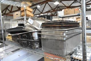 Stack of used kitchen baking trays and pans on metal shelves in an industrial setting. Auction tag visible.