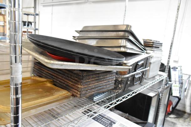Stack of assorted kitchen baking trays and pans on metal shelving, various materials and sizes, showing signs of use.