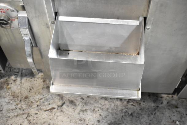 Commercial stainless steel popcorn machine with catch tray, visible wear, and operating instructions label on side.