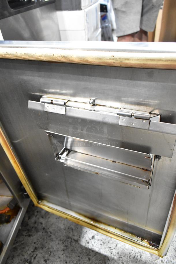 Stainless steel oven door with hinge mechanism, showing signs of wear and some rust along edges.