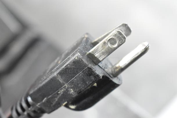 Close-up of a black two-prong electrical plug, showing signs of wear. No visible markings or labels.