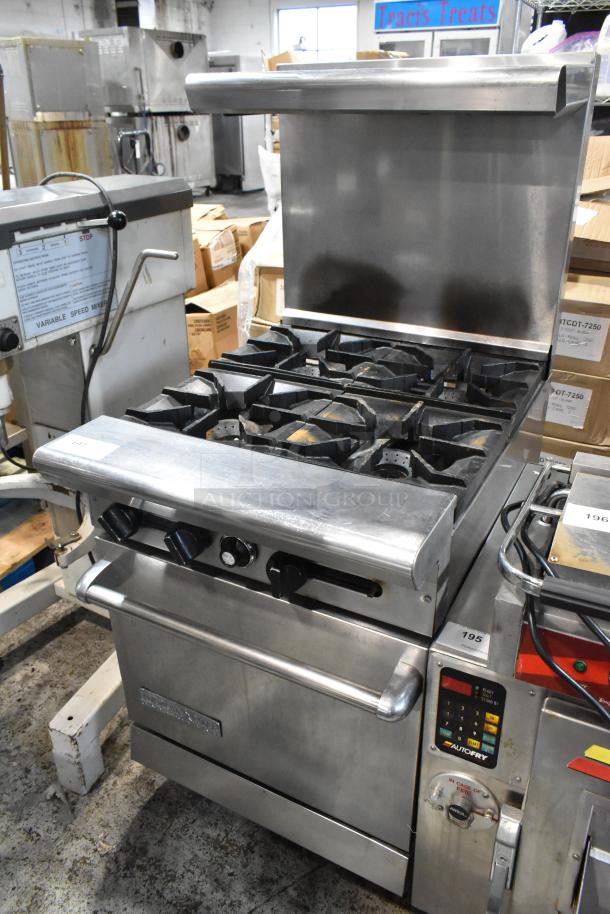 Commercial stainless steel gas range with six burners, oven, and splash guard. Features control knobs and temperature controls.