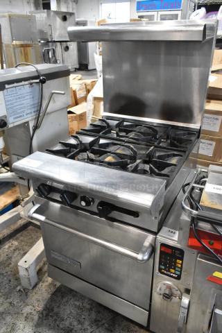 Commercial stainless steel gas range with six burners, oven, and splash guard. Features control knobs and temperature controls.