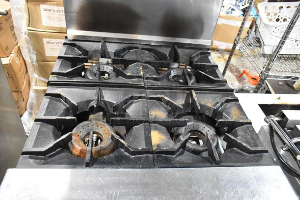 Commercial gas stovetop with six burners, showing signs of rust and wear. Ideal for restaurant use. No visible branding.
