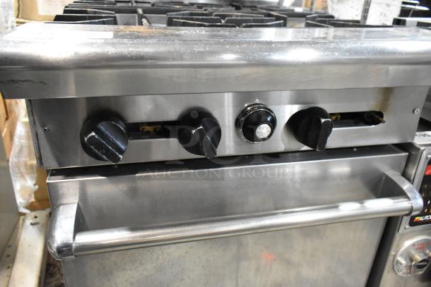 Commercial stainless steel gas range with four burners and three control knobs, showing moderate wear, ideal for industrial kitchens.