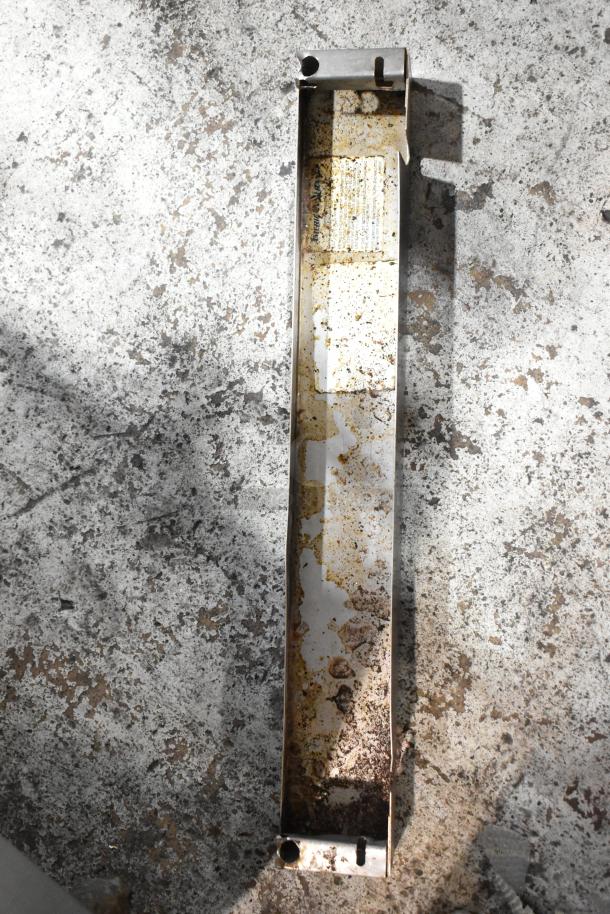 Rusty metal bracket with visible wear and corrosion, featuring a partially legible label inside, lying on a speckled surface.