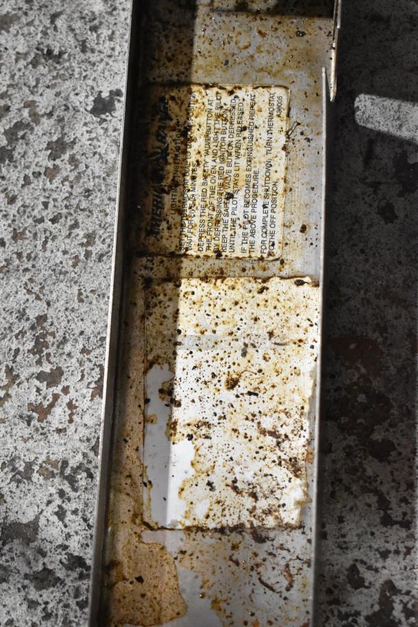 Rusty metal tray with visible wear and corrosion, featuring a partially readable label with safety instructions.
