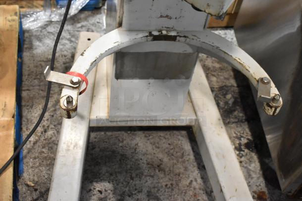 Industrial metal stand with two curved arms with bolts, showing surface rust and wear. Cables and a red tag attached.