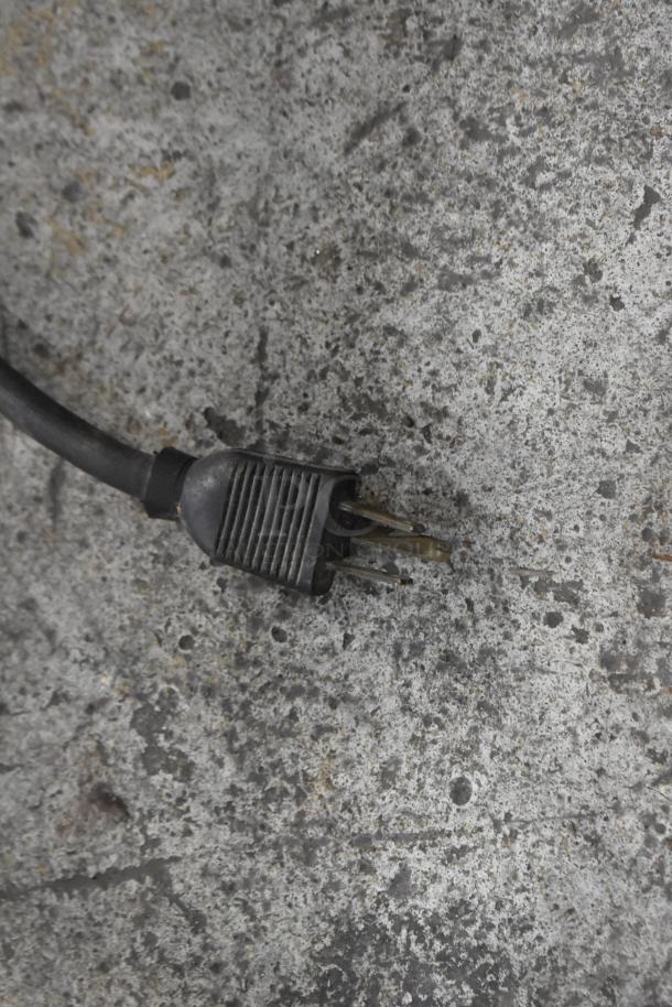 Black electrical plug with two metal prongs on a textured gray surface, showing wear and some discoloration.