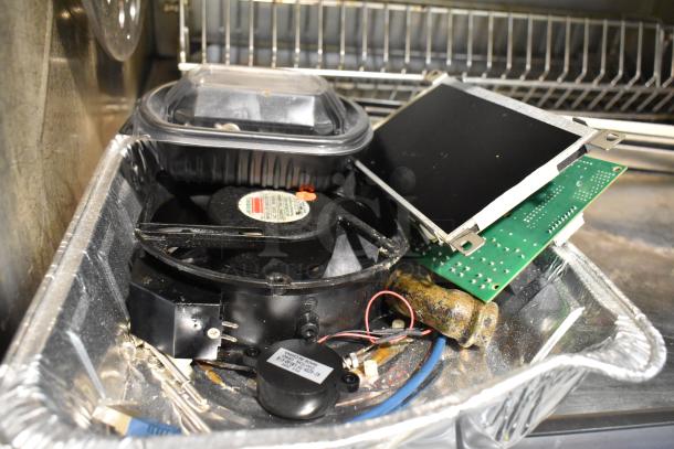 Tray of electronic parts, including a cooling fan, circuit board, and wires. Components appear used. Labels visible on fan.