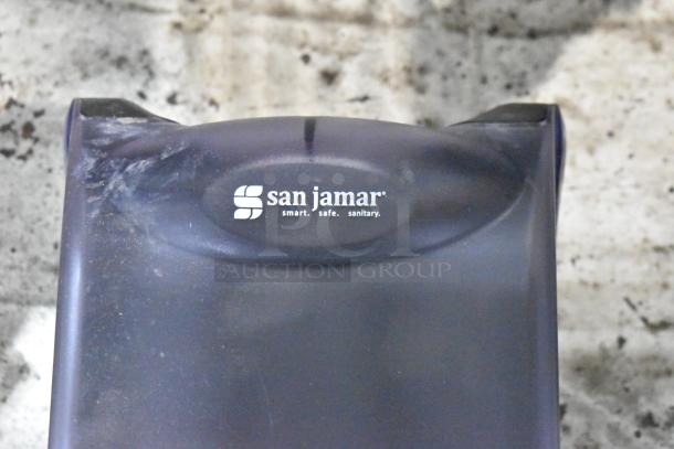 San Jamar paper towel dispenser, black, branded with "smart. safe. sanitary." text, slightly worn condition.