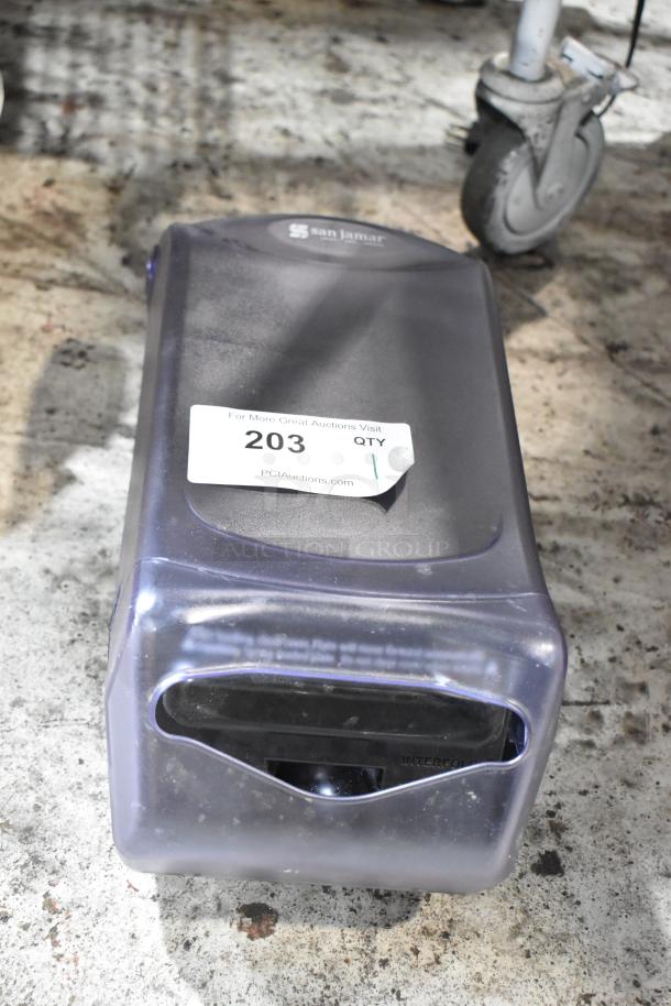 San Jamar paper towel dispenser, black plastic, used condition. Label indicates auction lot 203 by PCIAuctions.com.