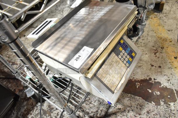 Digital weighing scale with keypad and stainless steel platform, tagged as item 204, in used condition on a metal cart.