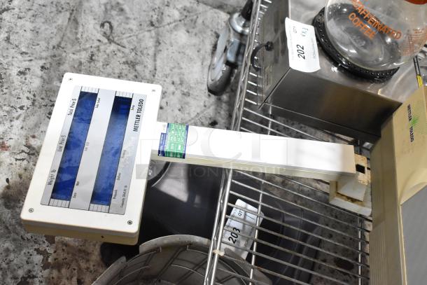 Mettler Toledo digital scale on metal cart, displays weight and total price. Visible wear, with tags indicating item 202.