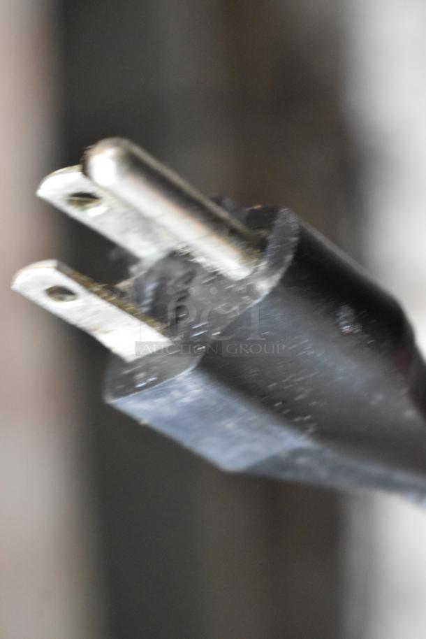 Close-up of a black electrical plug in used condition. Two metal prongs are visible; no labels or markings.