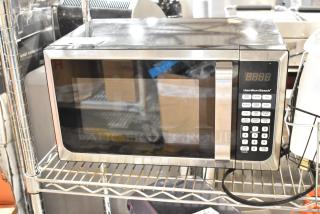 Hamilton Beach microwave, stainless steel finish, digital display, keypad with cooking presets, good condition, on shelf.