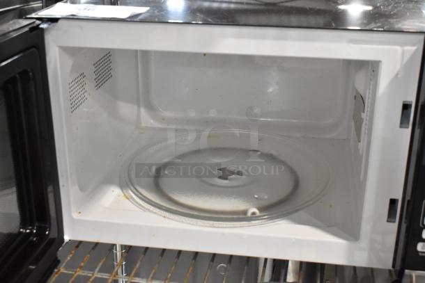 Open microwave interior with glass turntable, showing slight wear. White interior with ventilation holes. Auction tag visible.