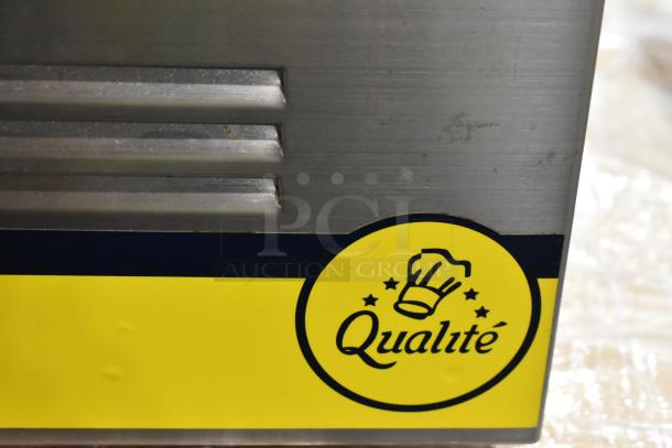 Metal appliance with "Qualité" logo on yellow label, stainless steel finish, vented panel, minor surface wear.