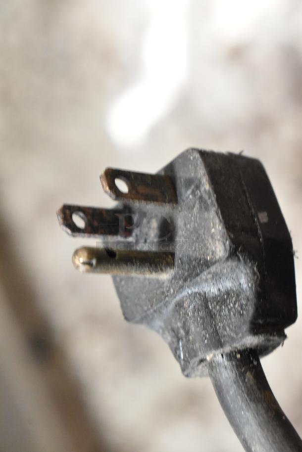 Worn three-prong electrical plug with visible corrosion and a frayed black cable, indicating possible functional issues.