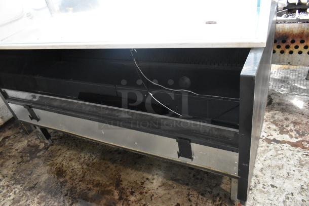 Commercial display fridge with metal frame and glass top, showing wear. Visible power cords; ideal for retail use.