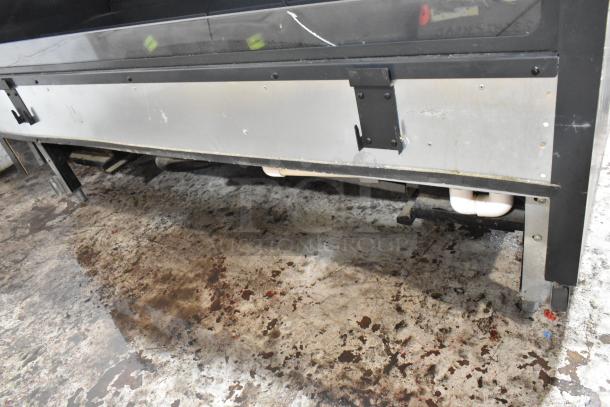 Commercial stainless steel cooler underside with visible pipes and brackets, showing signs of wear and surface rust.