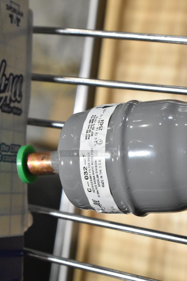 Gray refrigerant filter drier with label indicating model C-032-S, made in the USA, in new condition.