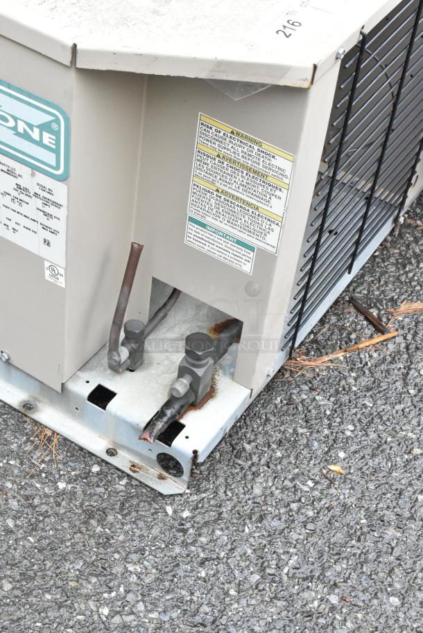 Outdoor HVAC unit with visible wiring and connectors, showing signs of rust. Warning labels detail electrical hazards.