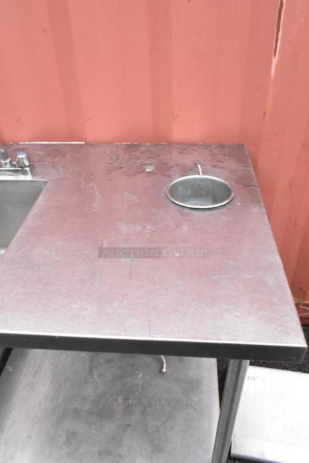 Stainless steel sink with side draining board, pre-owned with visible wear. Includes dual faucets and waste chute.